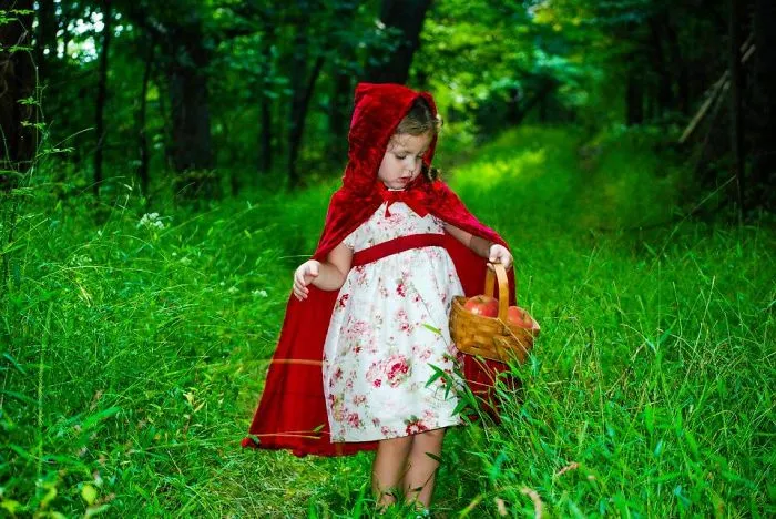 Young child in a red hooded cape and dress holding a basket, showcasing creative children's Halloween costume ideas outdoors.