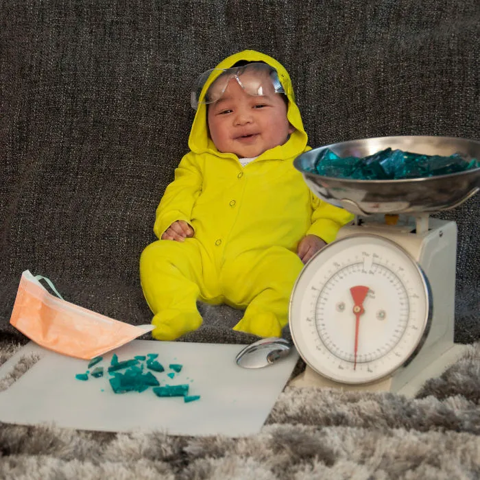 Baby wearing a yellow costume and goggles surrounded by props in a playful scene for children's Halloween costume ideas.
