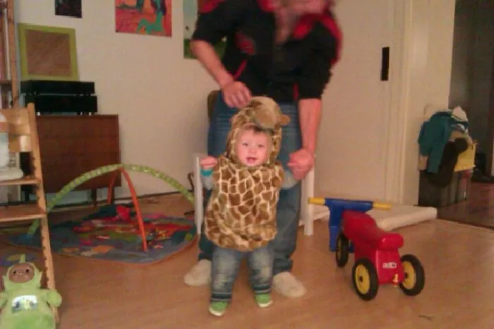 Toddler dressed in a giraffe costume learning to walk indoors, showcasing children's Halloween costume ideas for young kids.