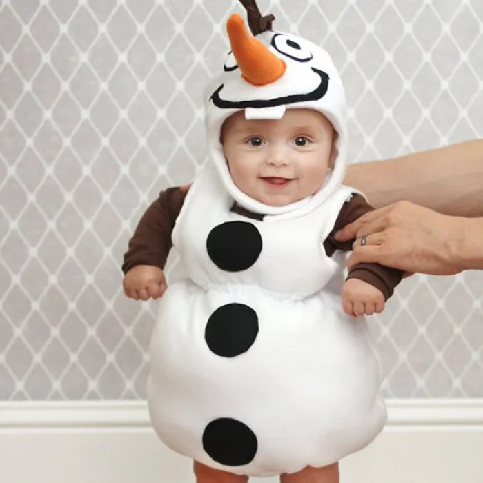 Baby dressed in a snowman Halloween costume smiling with adult hands supporting, showcasing children's Halloween costume ideas.