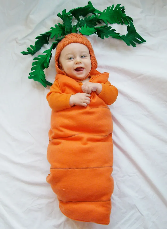 Baby dressed as a carrot lying on a white blanket, a cute example of children's Halloween costume ideas.