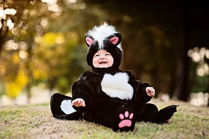 Baby dressed in a cute skunk costume sitting outdoors, perfect for children’s Halloween costume ideas celebration.