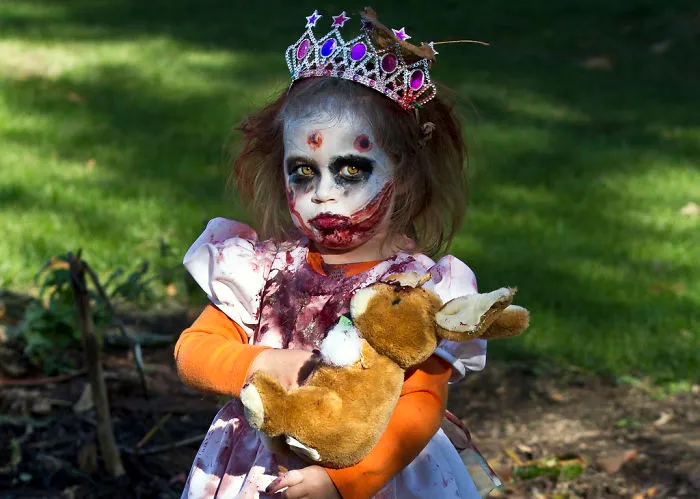 Child in creepy princess costume with detailed Halloween makeup holding a stuffed rabbit outdoors Halloween costume ideas.