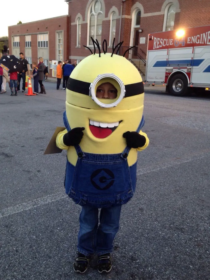 Child dressed as a Minion character in a creative children's Halloween costume ideas event outdoors near a rescue engine.