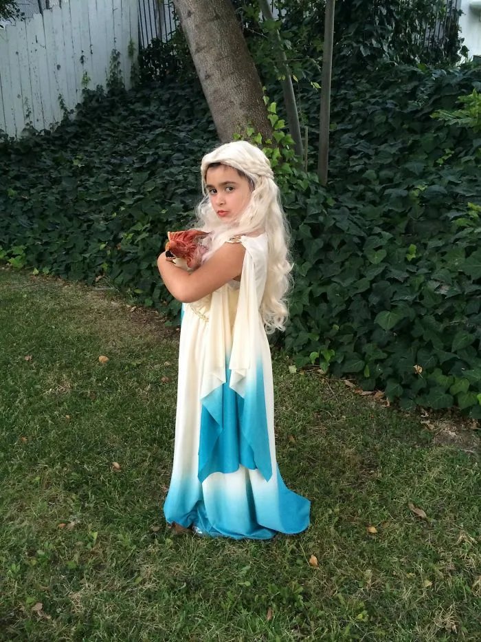 Child in a flowing blue and white costume holding a small furry animal outdoors for children's Halloween costume ideas.