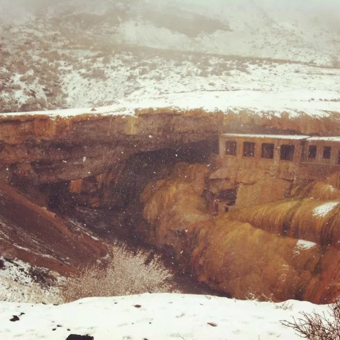 Mystical bridge carved into snowy rocky landscape with ancient stone structure nestled in rugged terrain.