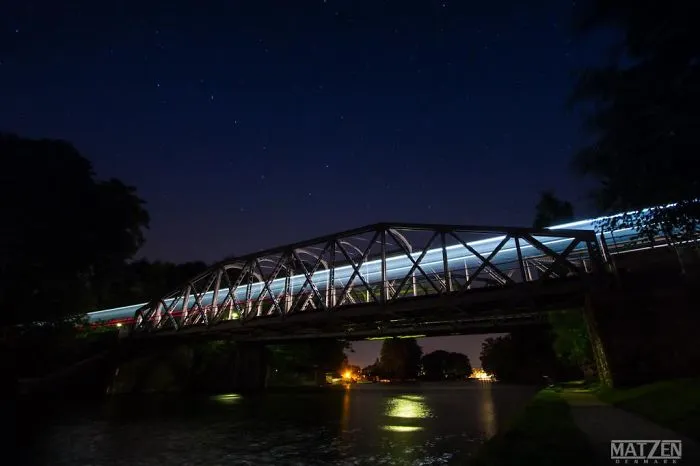 Mystical bridge at night with light trails crossing over water under a starry sky in a serene landscape.