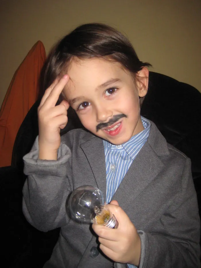 Young child in Halloween costume with fake mustache and suit holding a light bulb, representing creative children's Halloween costume ideas.