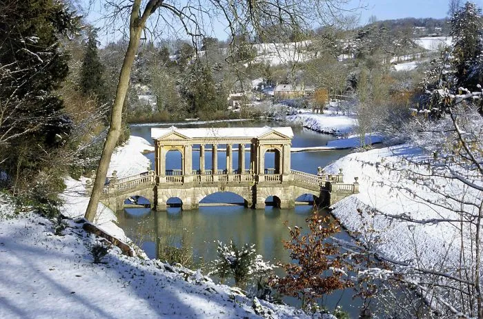 Stone bridge with classical columns over a river in a snowy landscape, showcasing mystical bridges in winter.