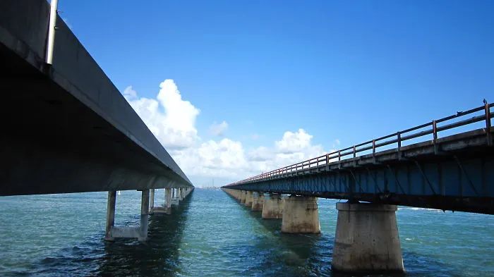 Two parallel mystical bridges extending over clear blue water under a bright sky with scattered clouds.