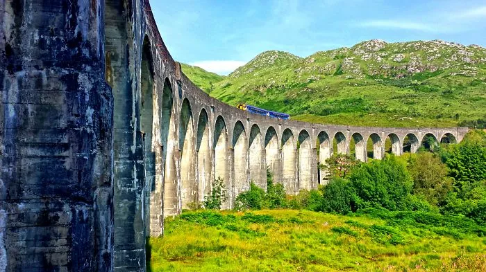 Stone arch bridge with a train passing through lush green hills, showcasing mystical bridges in a scenic landscape.