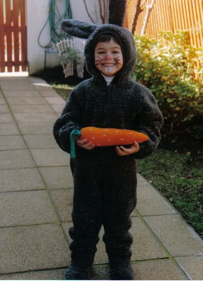 Child smiling in a black bunny costume holding a large carrot, perfect for children's Halloween costume ideas.