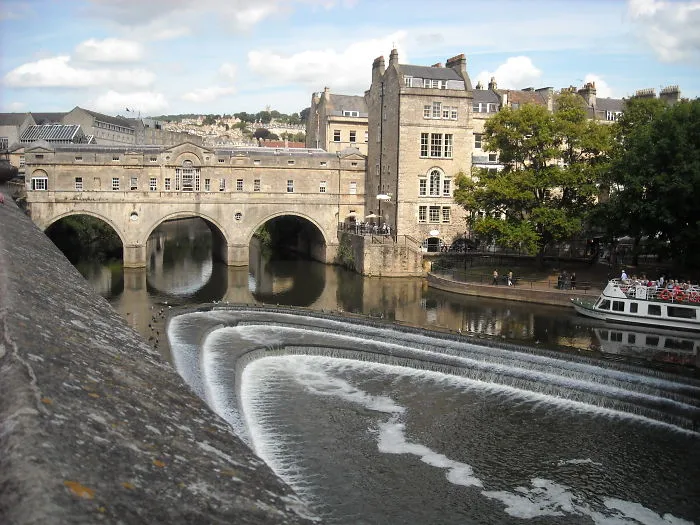 Historic stone bridge over river with cascading water and buildings, showcasing mystical bridges in a serene setting.