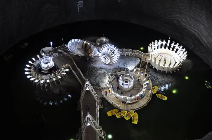 Mystical bridges and illuminated walkways over water inside a large dark cave with boats nearby at night.