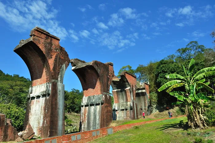Ancient mystical bridge ruins surrounded by greenery under a bright blue sky, evoking a sense of otherworldly adventure.