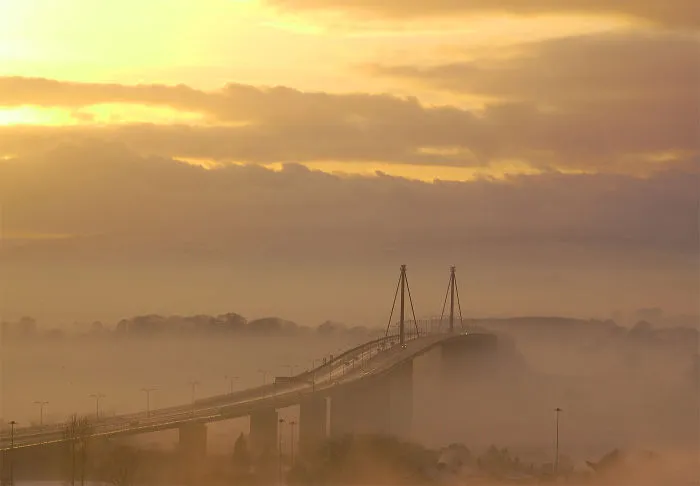 Foggy scene of a mystical bridge stretching into the mist under a golden sky at sunrise, creating an otherworldly atmosphere.