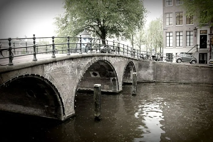 Historic mystical bridge with stone arches over calm water, surrounded by trees and urban buildings in a serene setting
