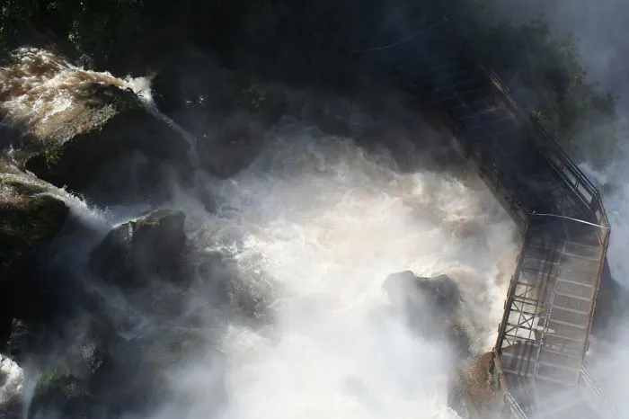 Wooden mystical bridge shrouded in mist over rushing river waters and dark rocks in a foggy natural landscape.