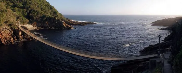 Suspension bridge over rocky coastline and deep blue sea, a mystical bridge that feels like a portal to another world.