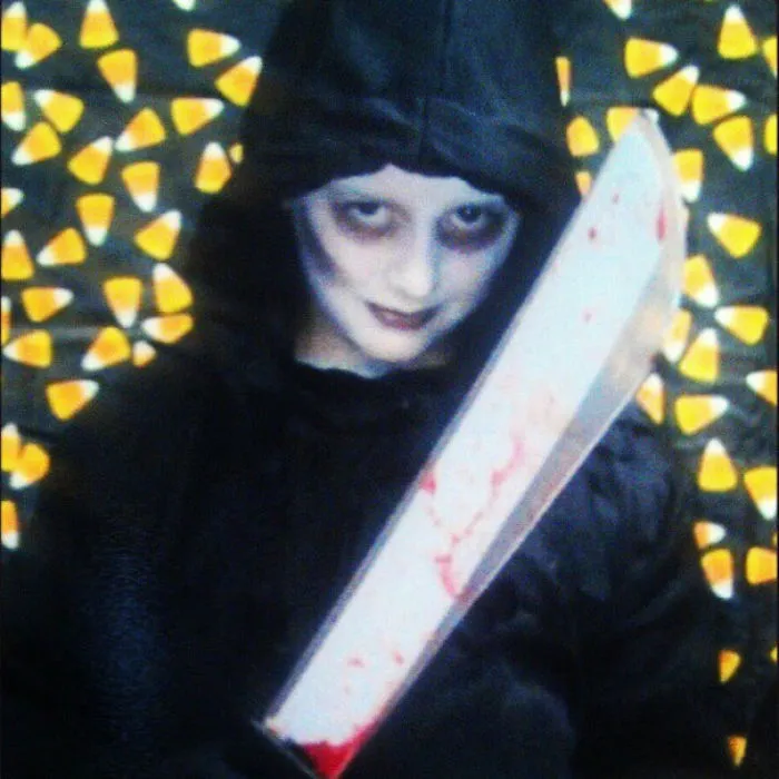 Child in creepy Halloween costume holding a bloodied machete, surrounded by candy corn for children's Halloween costume ideas.