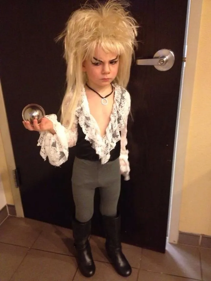 Child in an elaborate costume with wild blond hair, lace shirt, leggings, and boots holding a silver ball for children's Halloween costume ideas.