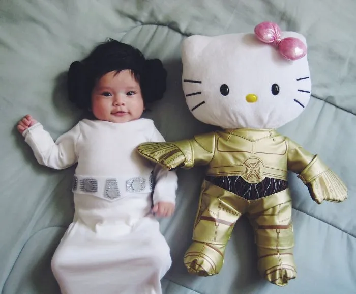 Baby dressed in a creative Halloween costume lying next to a Hello Kitty doll in gold outfit for children's Halloween costume ideas.