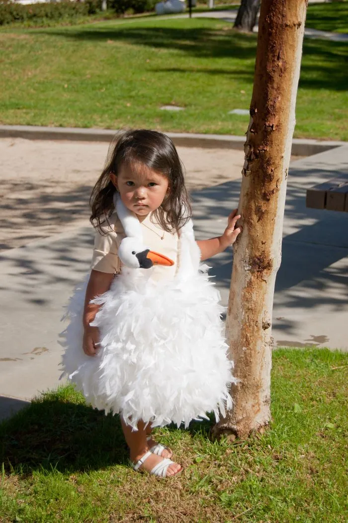 Young child wearing a white swan costume standing outdoors near a tree, showcasing children's Halloween costume ideas.