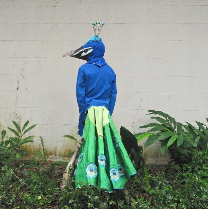 Child in a colorful peacock costume standing outdoors with greenery, showcasing creative children's Halloween costume ideas.