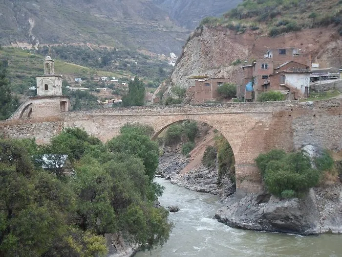 Ancient stone bridge over a river surrounded by mountains and greenery, showcasing mystical bridges in a serene landscape.