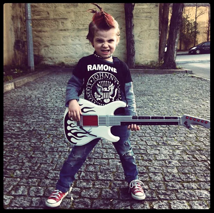 Child dressed in a punk rock costume holding a guitar outside, showcasing creative children's Halloween costume ideas.