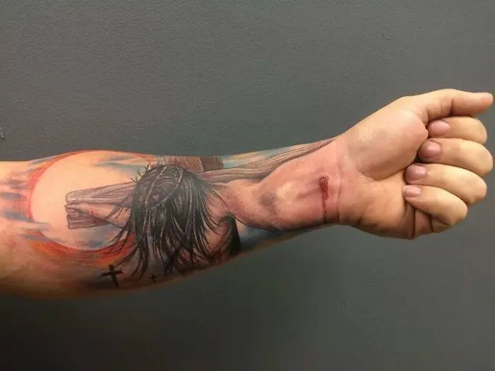 3D tattoo of Jesus on a cross on a man's forearm, creating a mind-twisting visual effect.