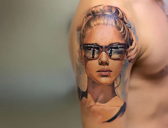 3D tattoo of a woman with sunglasses on an arm, showcasing realistic art.