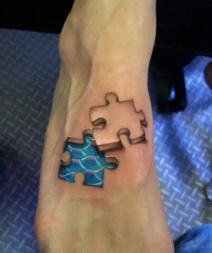 3D tattoo of puzzle pieces on a foot, with one piece revealing a blue pattern beneath the skin.