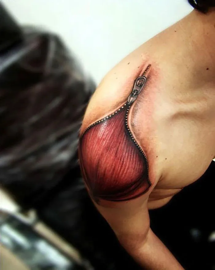 3D tattoo of a realistic unzipped zipper revealing muscle tissue on shoulder.