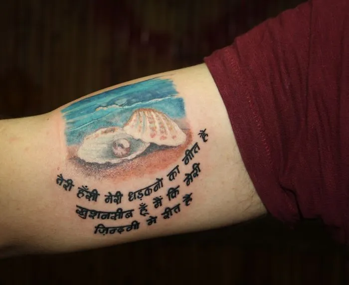 3D tattoo of a seashell with Hindi script on an arm.