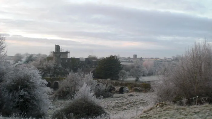 Frost-covered mystical stone bridge and castle ruins in a foggy landscape during early morning winter.