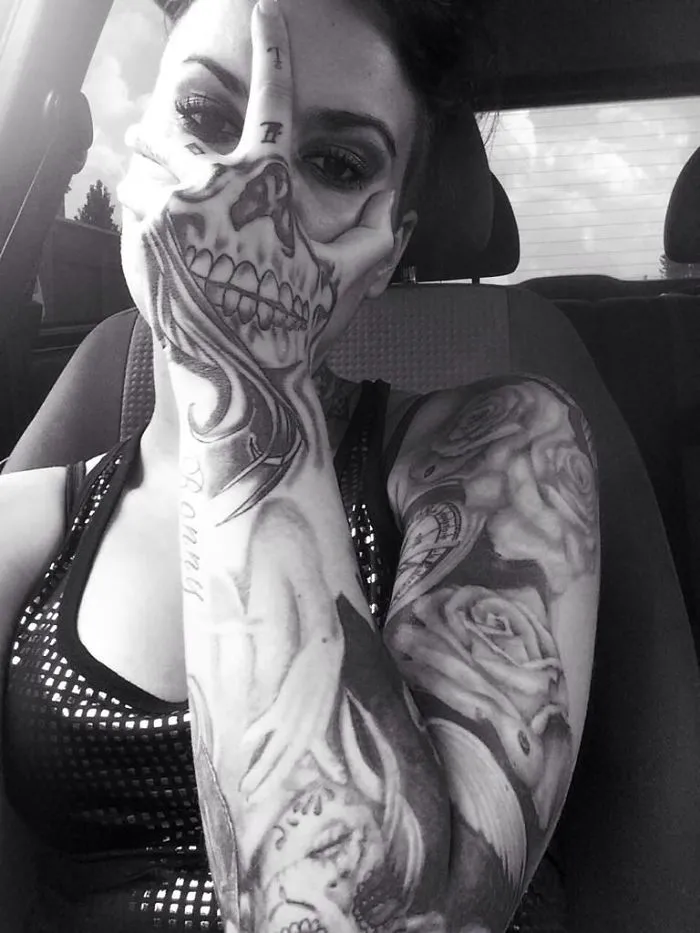 Close-up of a person with a detailed 3D skull tattoo on their hand, holding it over half their face.