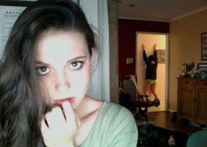 Woman posing in foreground with a surprising scene in the background when you see it.
