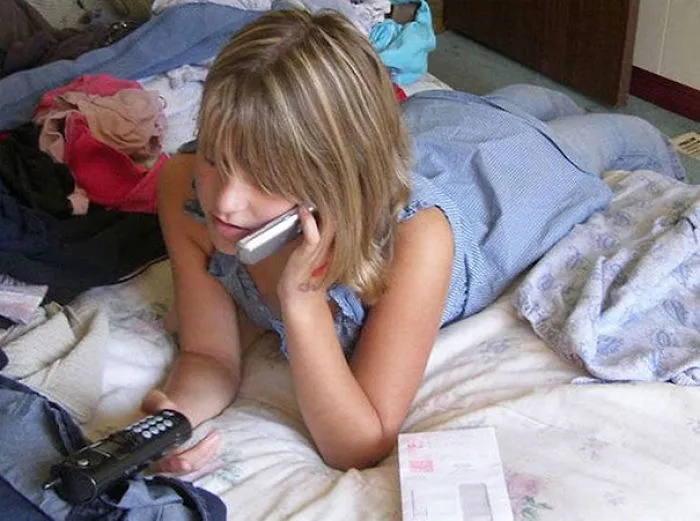 Girl on bed using a phone, with unexpected detail in the background that might surprise viewers.