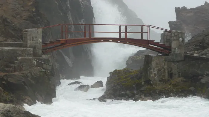 Mystical bridge over rocky waters with misty cliffs, creating an enchanting atmosphere in a remote natural setting.
