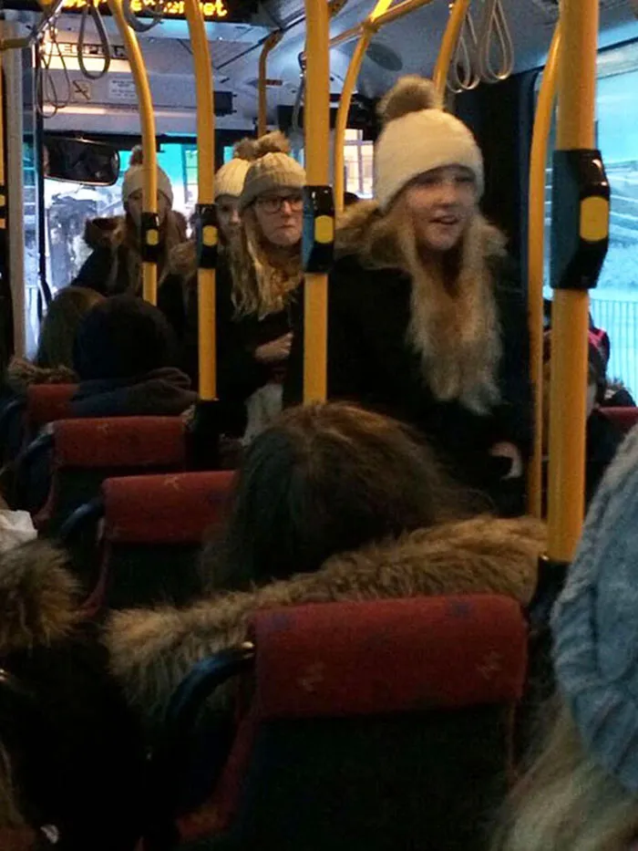 4 girls standing in the bus and wearing similar winter hats and clothes