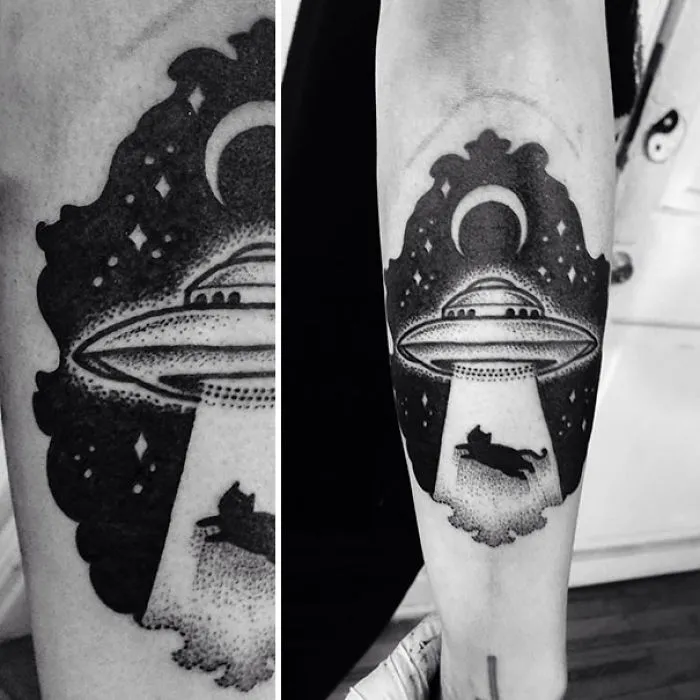 Creative cosmic arm tattoo with UFO and cat being abducted under a starry sky.