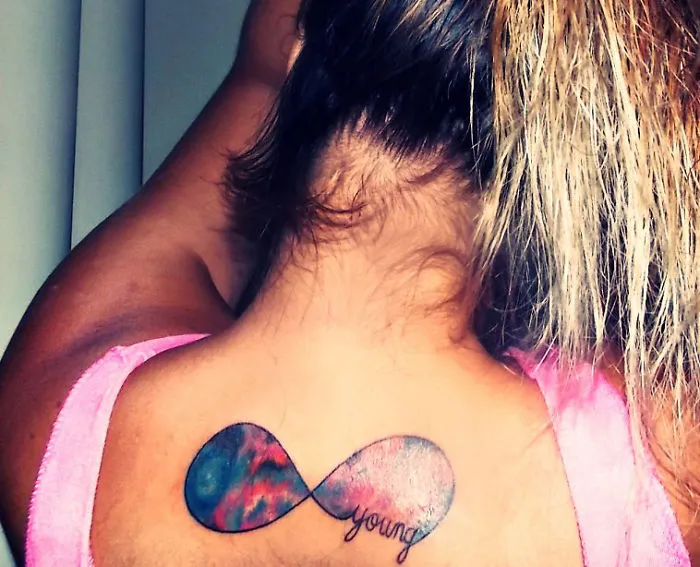 Colorful cosmic tattoo of an infinity symbol on a person's neck, featuring a galaxy design and the word "young."
