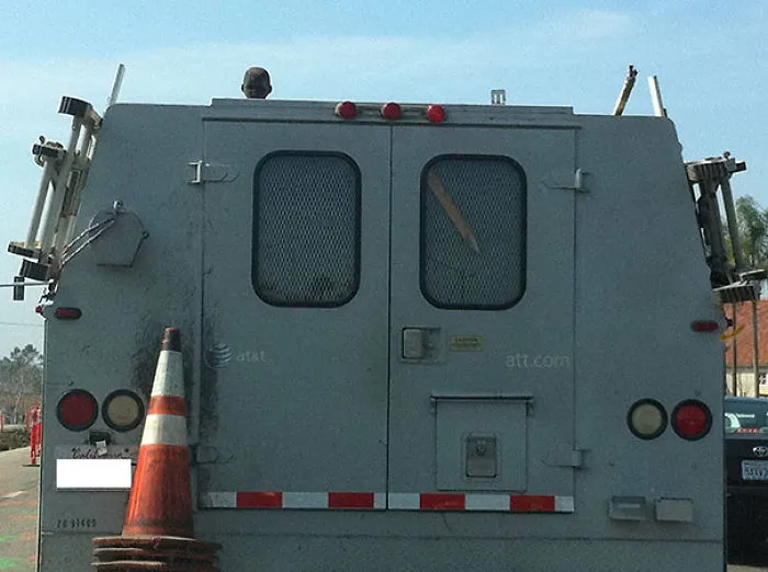 A head peeks over the roof of a gray van, creating an unexpected and humorous scene on the road.
