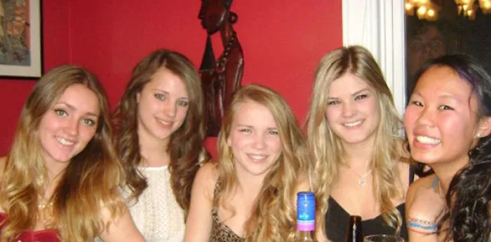 Group of friends smiling at a party, hidden face in the background creating a humorous surprise.