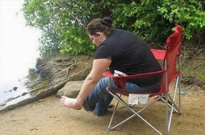 Woman sitting on a red chair by a riverbank, adjusting her shoe with a surprising detail in the background.