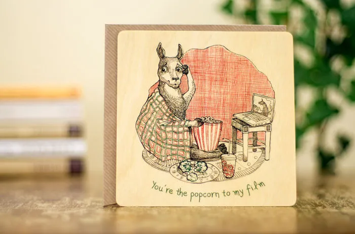 Unconventional Valentine's Day card featuring a llama wrapped in a blanket with popcorn by a TV.