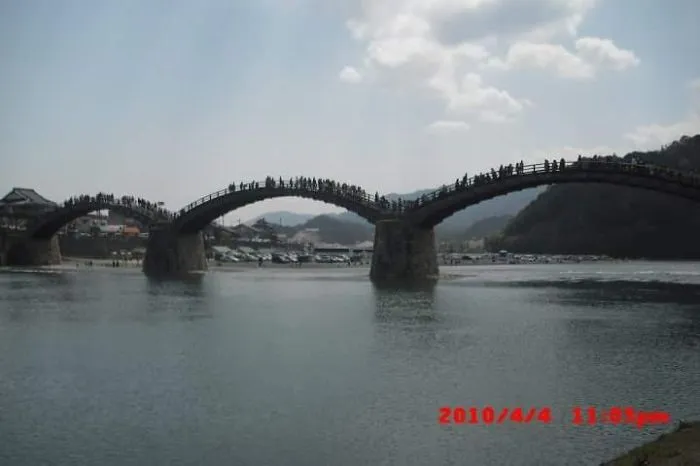Stone arch bridge over calm water with people walking, creating a mystical bridge scene in a serene landscape.