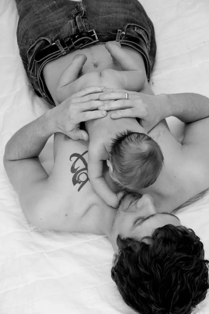 Tattooed parent lying down, holding baby on chest, showcasing a tender moment together.