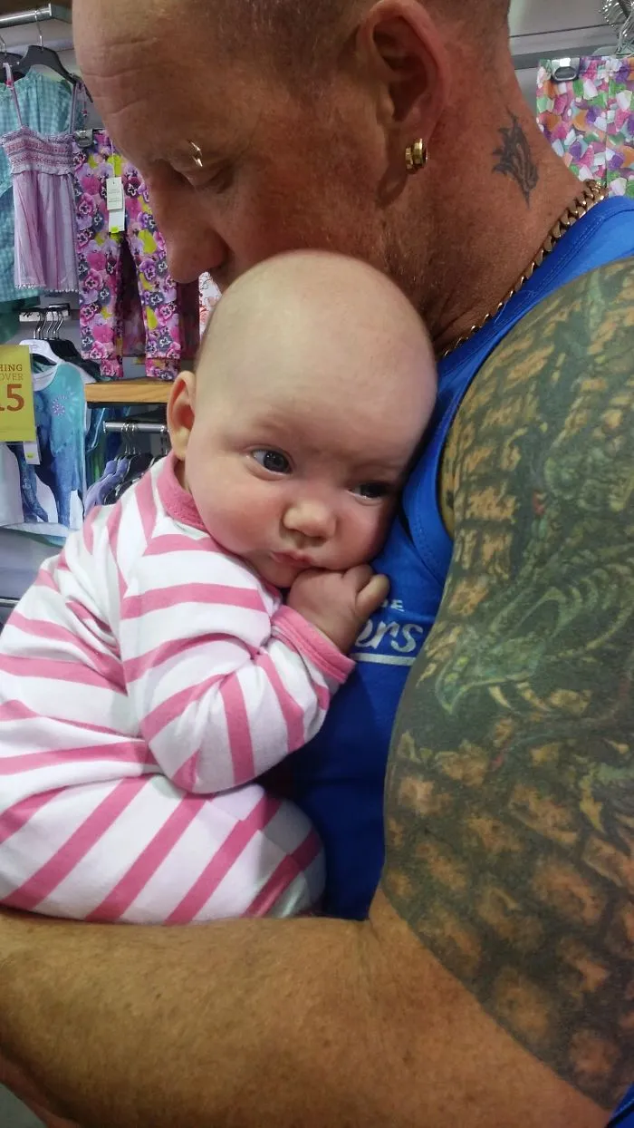 Tattooed parent gently holding baby in a striped onesie, showcasing their close bond together.